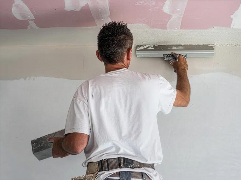 Maler trägt Farbe mit der Rolle gleichmäßig auf eine weiße Wand auf